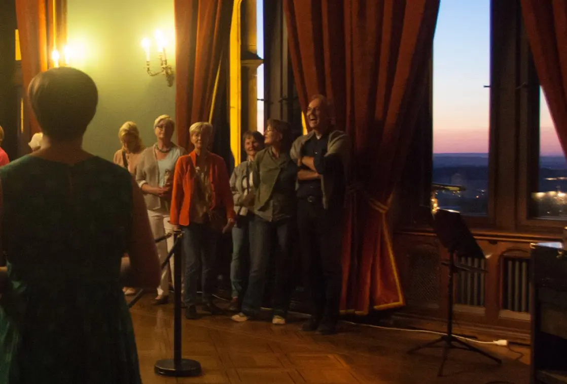 Gruppe bei einer Führung im Schloss in einem eleganten Raum mit roten Vorhängen und Wandleuchtern